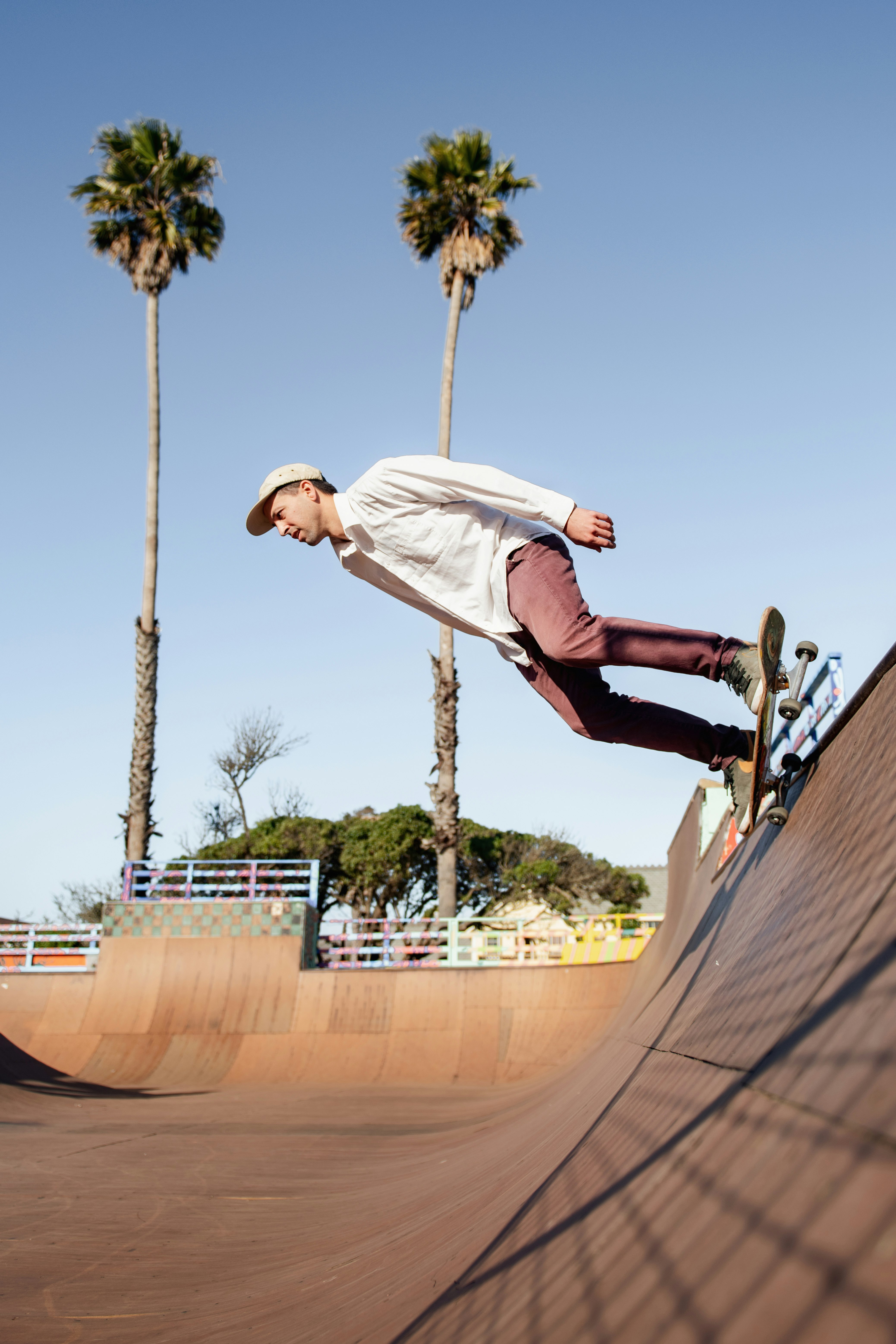 man in white t-shirt and blue denim jeans jumping on brown wooden skateboard ramp