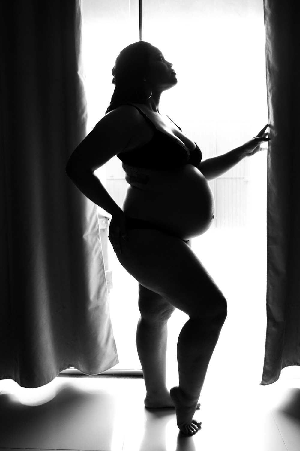 woman in black brassiere and panty standing beside curtain