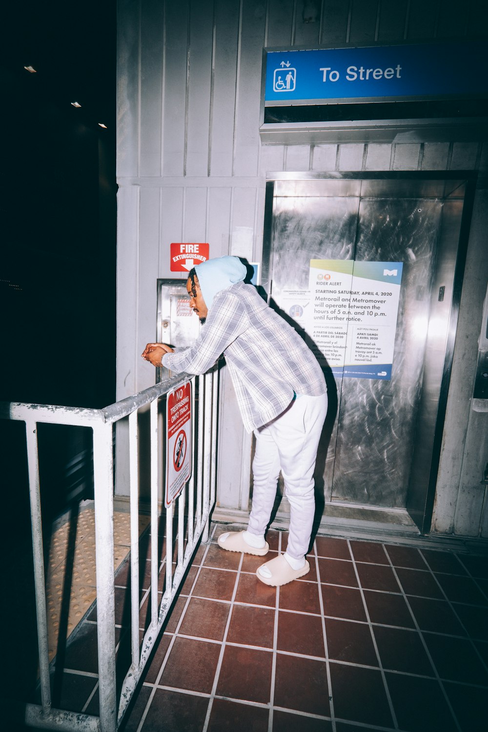 Hombre con sudadera con capucha gris y pantalones grises de pie junto a la valla de madera blanca