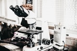 A close-up of a microscope with slides and laboratory equipment in a bright setting.