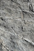 A detailed view of rough stone surface with visible natural textures, cracks, and vein-like patterns running across it.