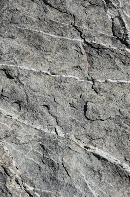 A detailed view of rough stone surface with visible natural textures, cracks, and vein-like patterns running across it.