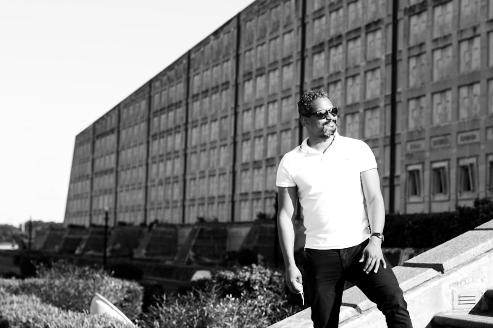 man in white crew neck t-shirt and black pants standing near building during daytime