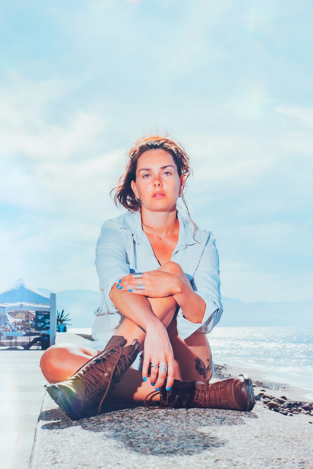 woman in blue button up shirt and brown leather boots sitting on beach during daytime