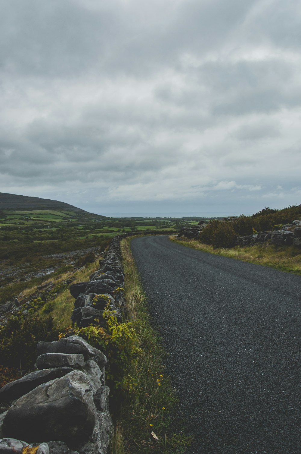 gray asphalt road between green grass field under white cloudy sky during daytime