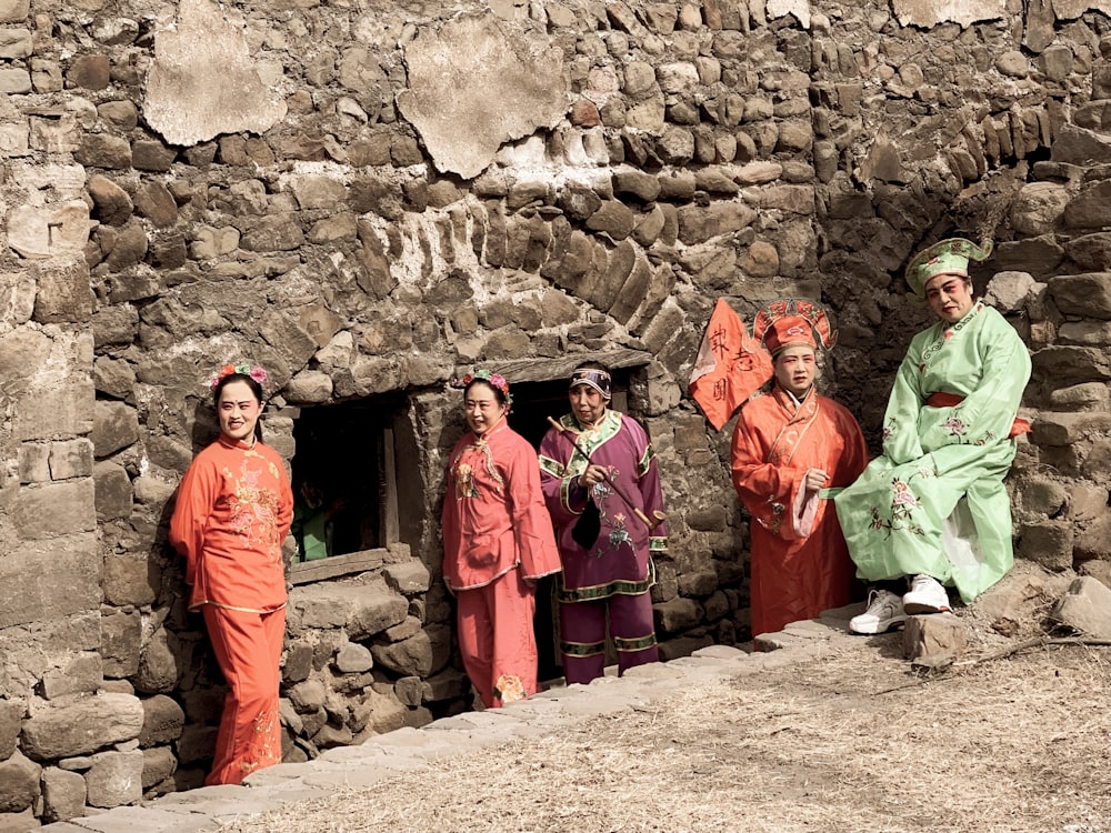 3 men in green robe standing beside brown brick wall during daytime