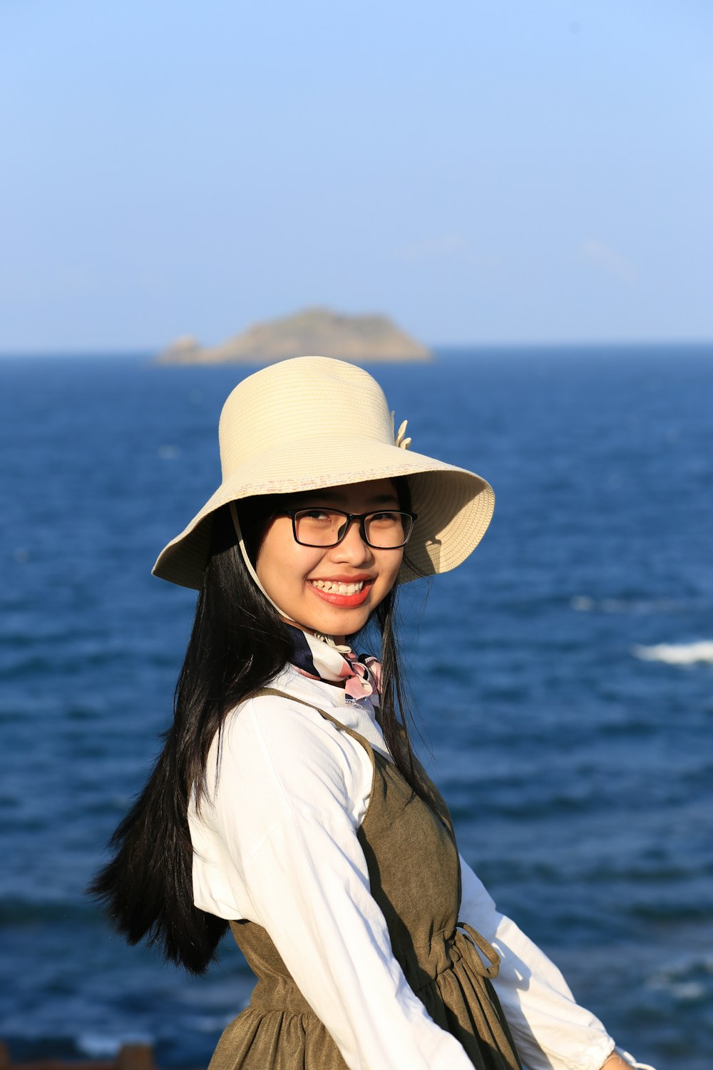 a woman wearing a hat and glasses standing near the ocean