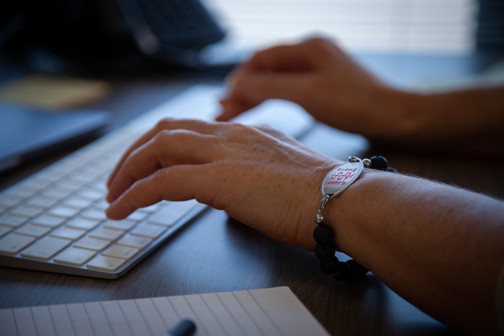 Persona que lleva un reloj de pulsera de eslabones plateados que sostiene el teclado de Apple