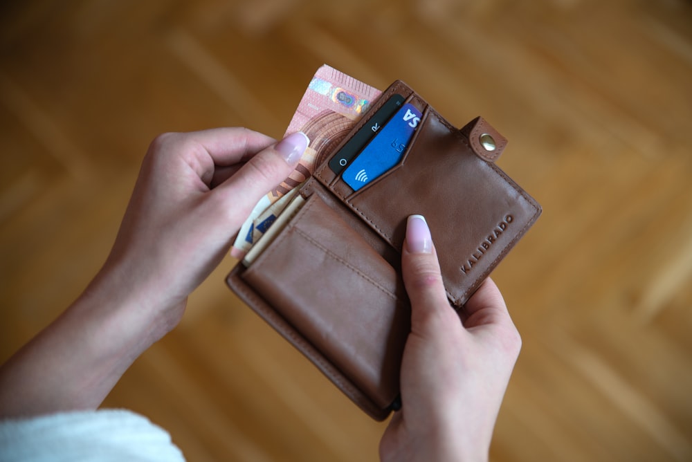 persona sosteniendo una billetera de tarjeta de cuero marrón