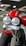 A close-up view of a motorcycle featuring dual round headlights, a prominent red fuel tank, and a sturdy front suspension. The motorcycle has a modern and robust design with a focus on the front wheel and tire. The showroom setting provides a sleek and polished look.