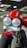 A close-up view of a motorcycle featuring dual round headlights, a prominent red fuel tank, and a sturdy front suspension. The motorcycle has a modern and robust design with a focus on the front wheel and tire. The showroom setting provides a sleek and polished look.