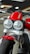A close-up view of a motorcycle featuring dual round headlights, a prominent red fuel tank, and a sturdy front suspension. The motorcycle has a modern and robust design with a focus on the front wheel and tire. The showroom setting provides a sleek and polished look.