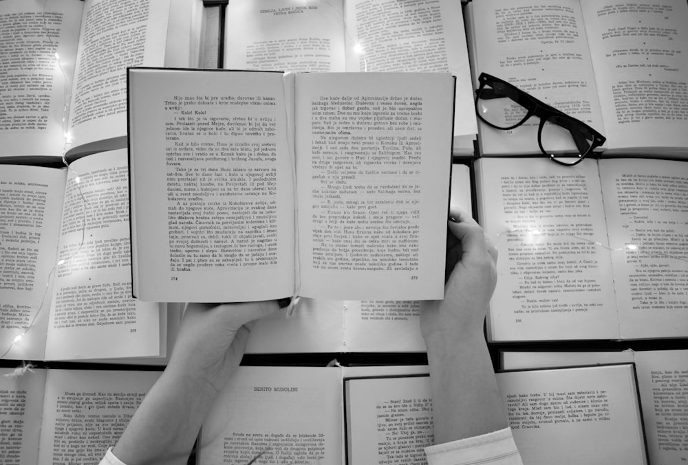 person holding book page with black frame eyeglasses