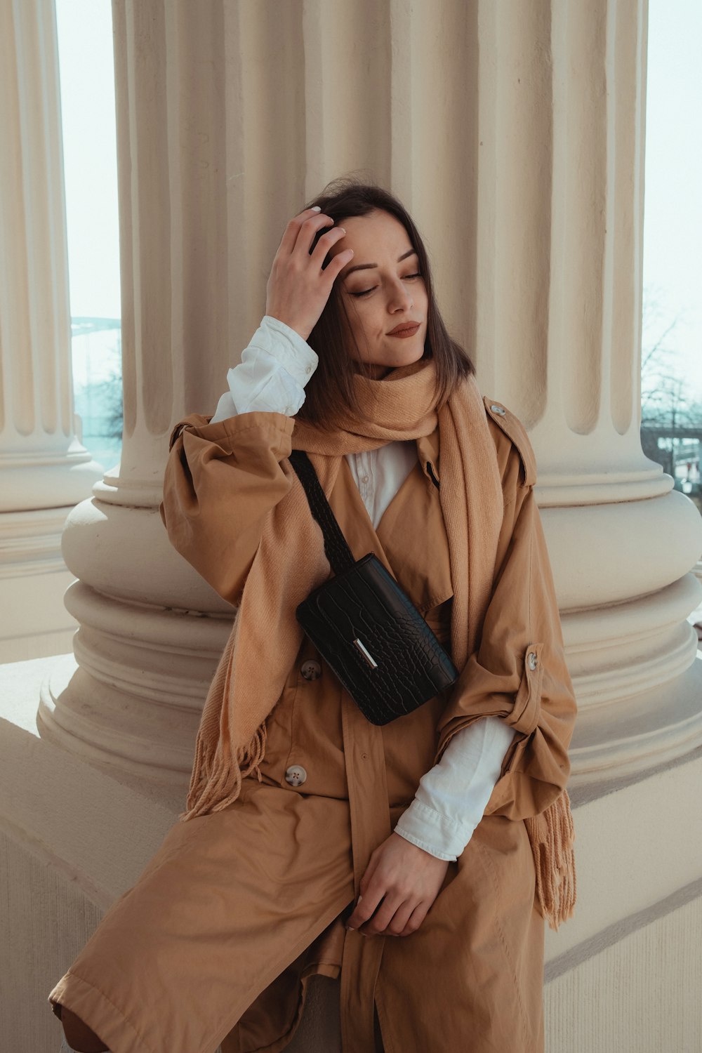 woman in brown coat holding black leather sling bag