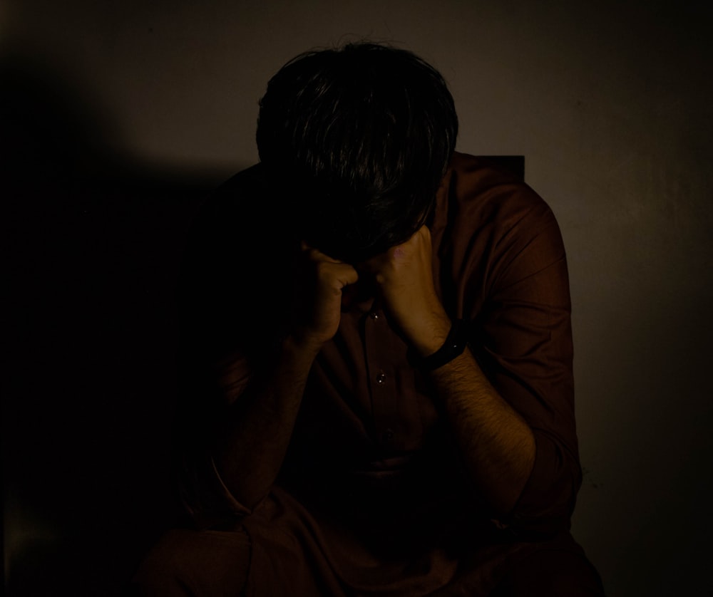 man in brown shirt covering his face