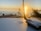 A sunset over the ocean is visible in the background, casting a warm glow. In the foreground, a laptop with a recognizable logo is placed on a wooden surface, next to a wireless antenna device. Tall grasses are silhouetted against the sky, adding a natural touch to the scene.
