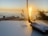 A sunset over the ocean is visible in the background, casting a warm glow. In the foreground, a laptop with a recognizable logo is placed on a wooden surface, next to a wireless antenna device. Tall grasses are silhouetted against the sky, adding a natural touch to the scene.
