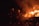 Two firefighters in protective gear are using a hose to extinguish a car engulfed in flames. Sparks and smoke fill the air, highlighting the intensity of the fire.
