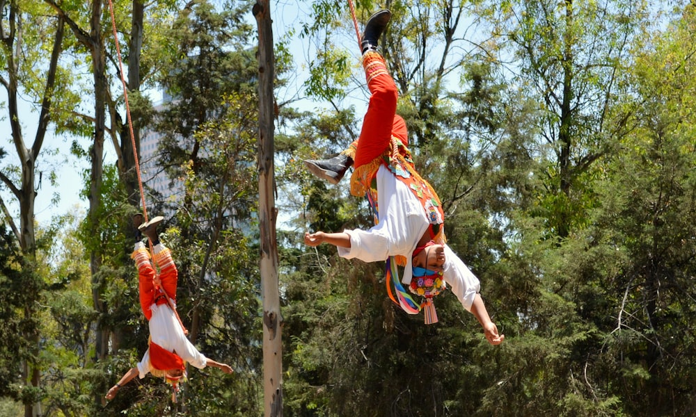 man in red t-shirt and white shorts jumping on brown wooden post during daytime