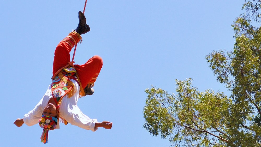 Hombre con chaqueta roja y pantalones blancos saltando en el aire bajo el cielo azul durante el día