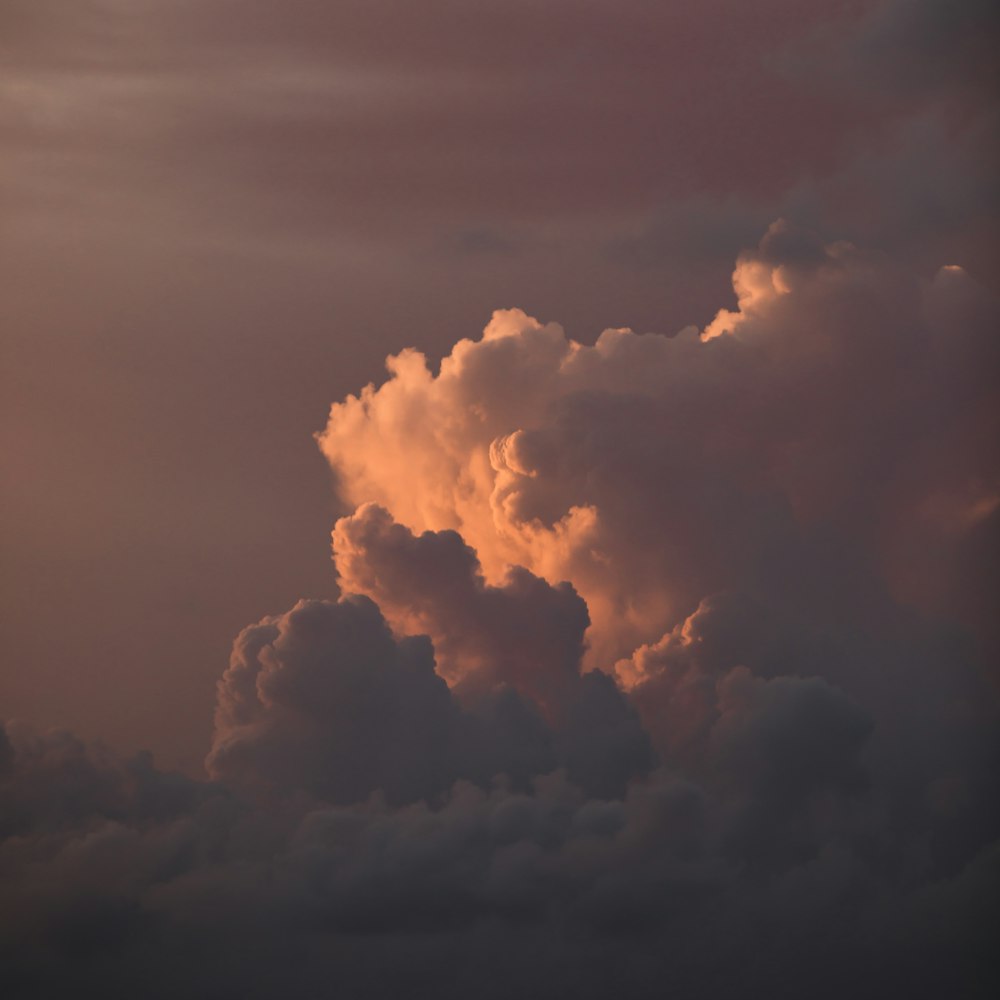 a plane flying through a cloudy sky at sunset