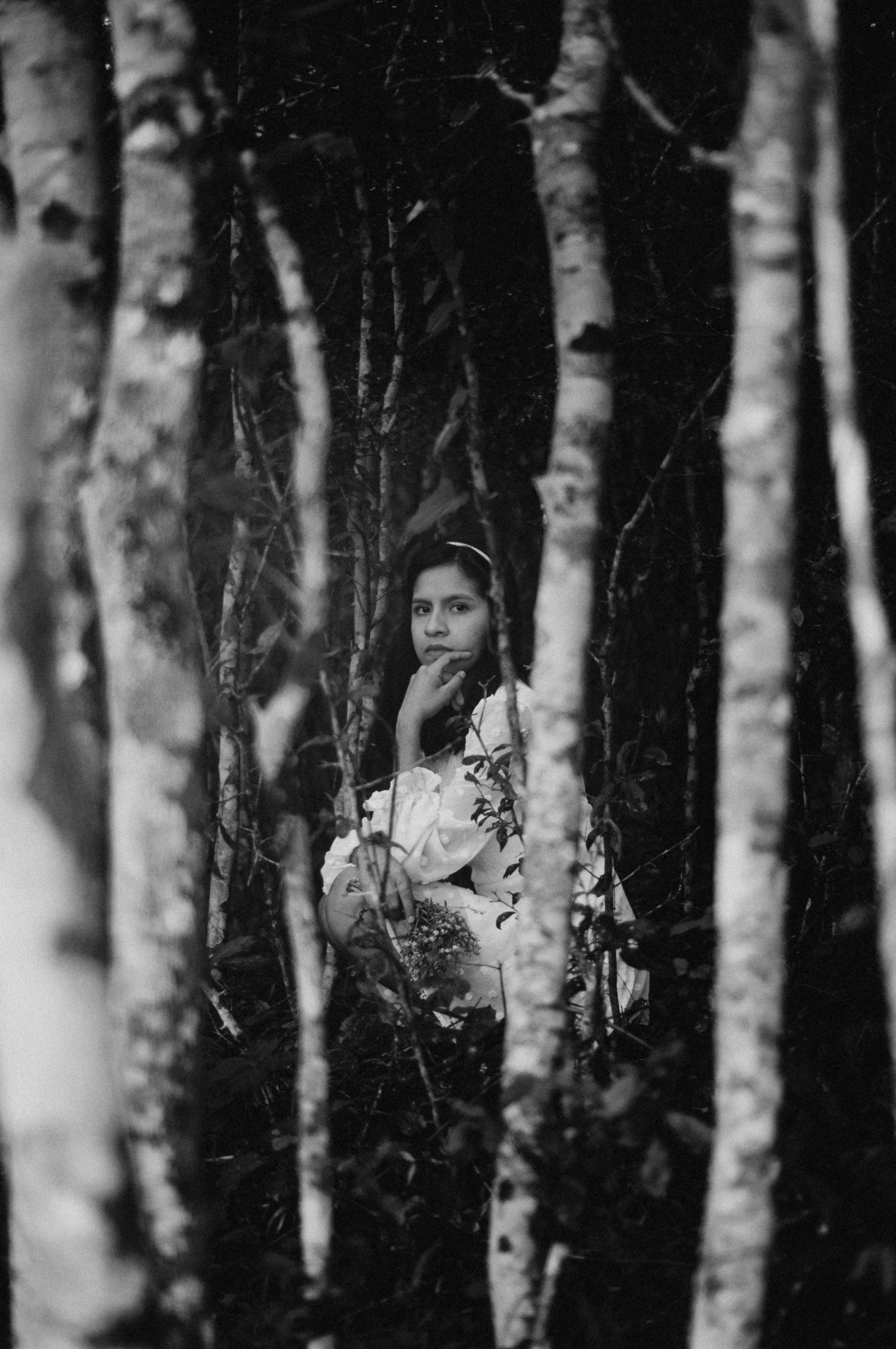 grayscale photo of woman in white dress standing in the middle of the forest
