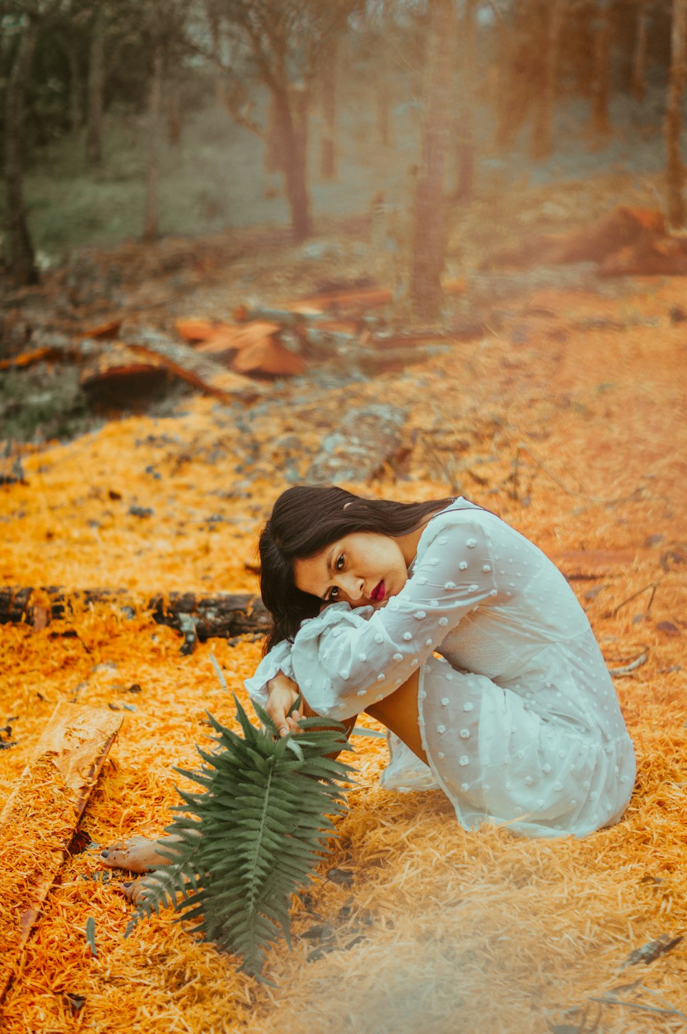 girl in white long sleeve dress lying on ground covered with dried leaves