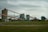 An industrial facility with multiple large, connected structures and conveyor belts spread across a grassy area under an overcast sky.