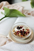 A cozy breakfast scene featuring a bowl of Greek yogurt topped with nuts and berries on a cream-toned table surface.