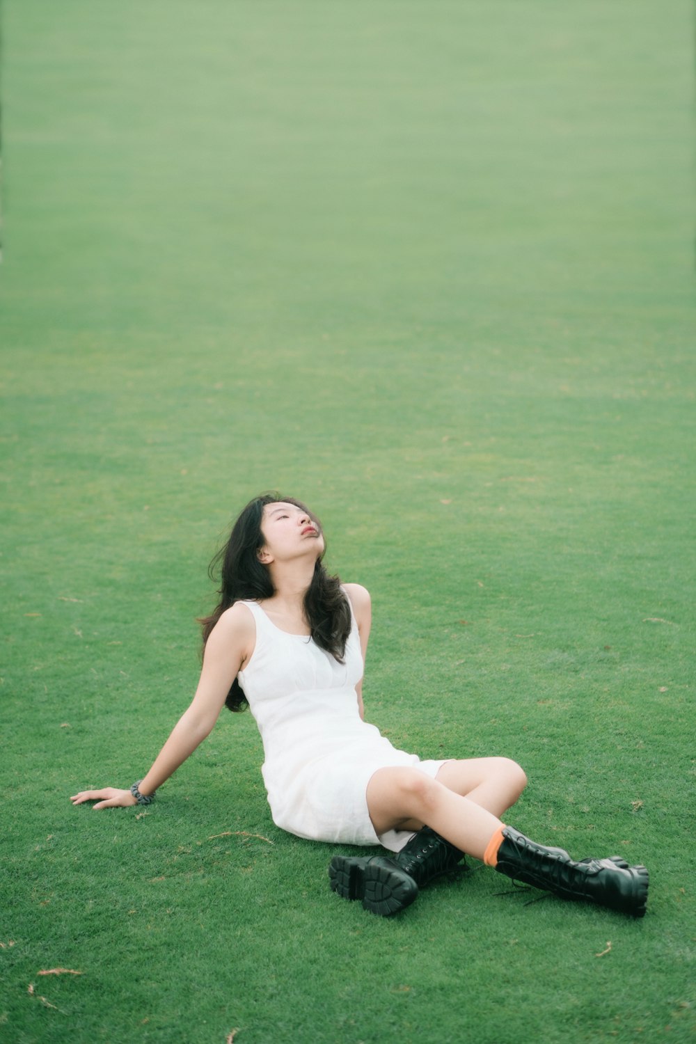 woman in white tank top and black shorts sitting on green grass field