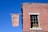 A red brick building with a rectangular window partially covered by a sign inside that reads 'DEFUND THE POLICE'. There is a brown banner hanging outside that reads 'De Stefano's Steak & Chops'. A street sign on the corner of the building displays 'CONSELYEA ST'. The sky is clear and blue.