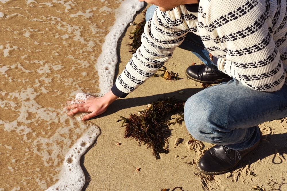 person in white and black long sleeve shirt and blue denim jeans sitting on brown sand