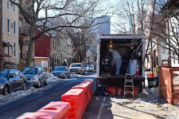 man in a biohazard hazmat suit standing in a white box truck with orange road barriers nearby
