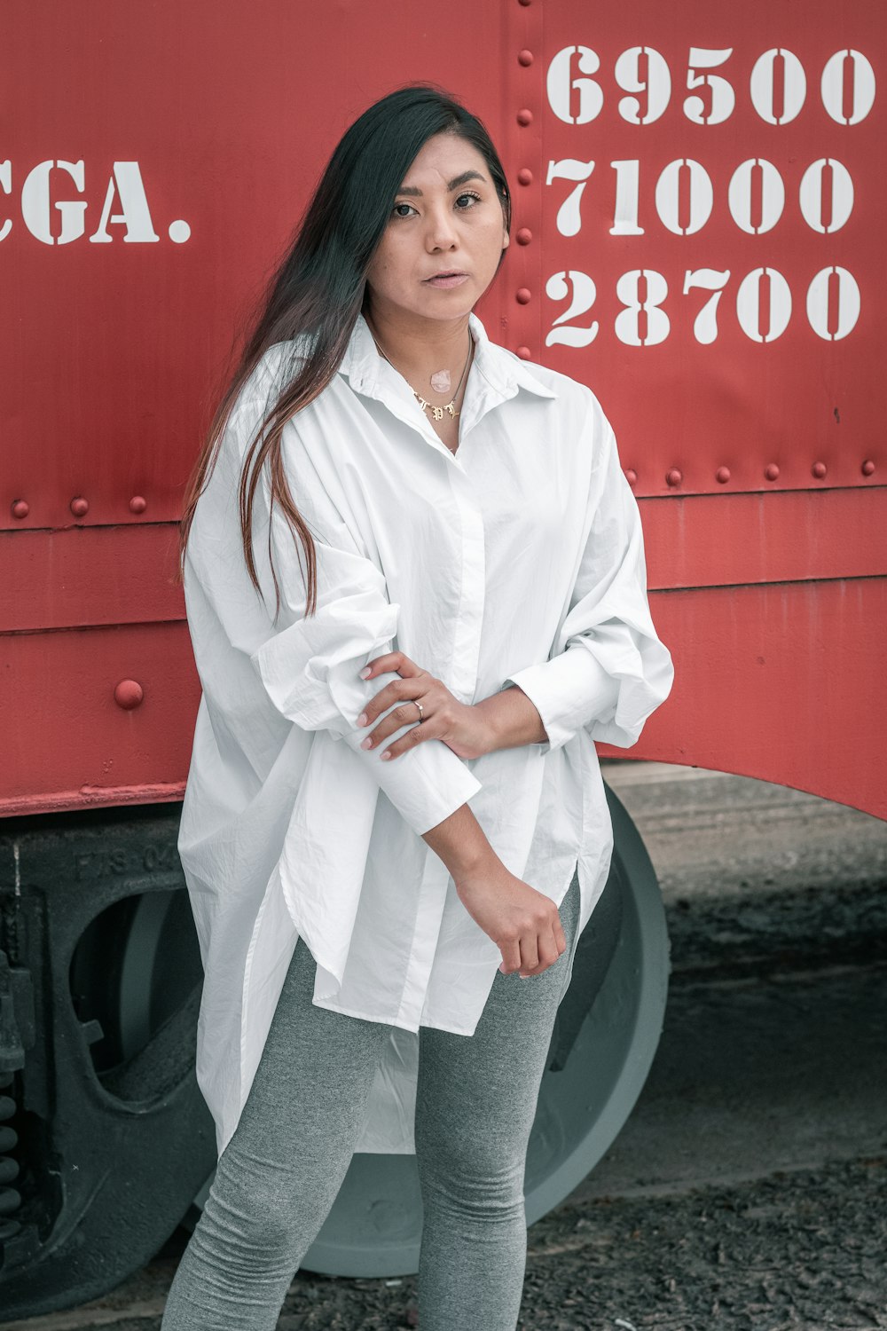 Femme en chemise à manches longues boutonnée blanche debout à côté d’une voiture rouge et noire