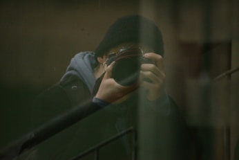 man in gray jacket holding black framed eyeglasses