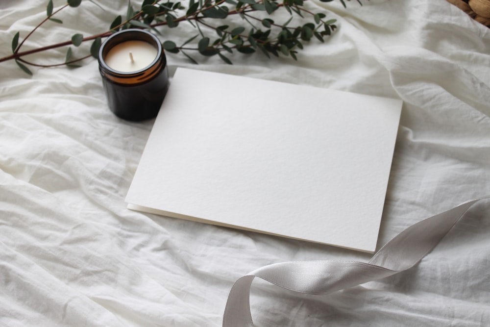 Papel de impresora blanco junto a taza de cerámica negra sobre textil floral blanco y verde