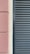 A close-up view of a building facade features a section of textured pinkish-brown plaster next to a cream-colored surface. Adjacent to these is a set of dark gray louvered shutters, creating a stark contrast between the smooth, modern surface and the textured, traditional wall.