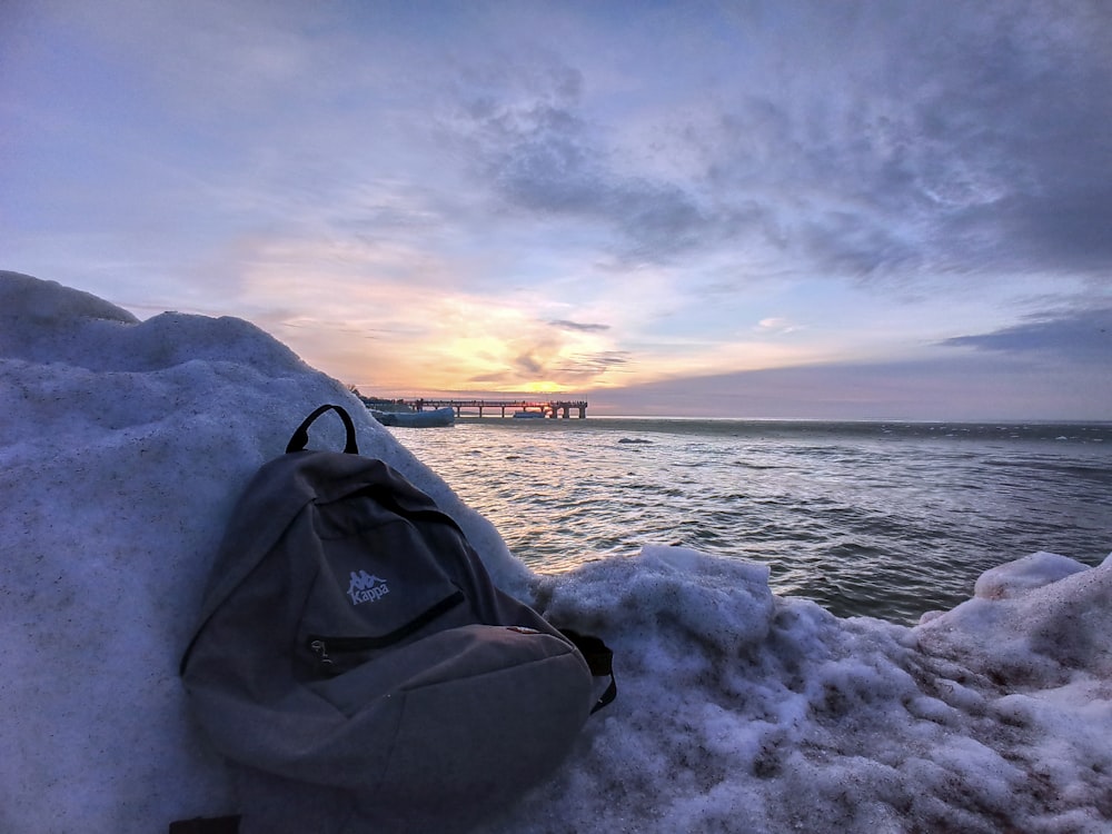 black leather backpack on gray rock near body of water during daytime