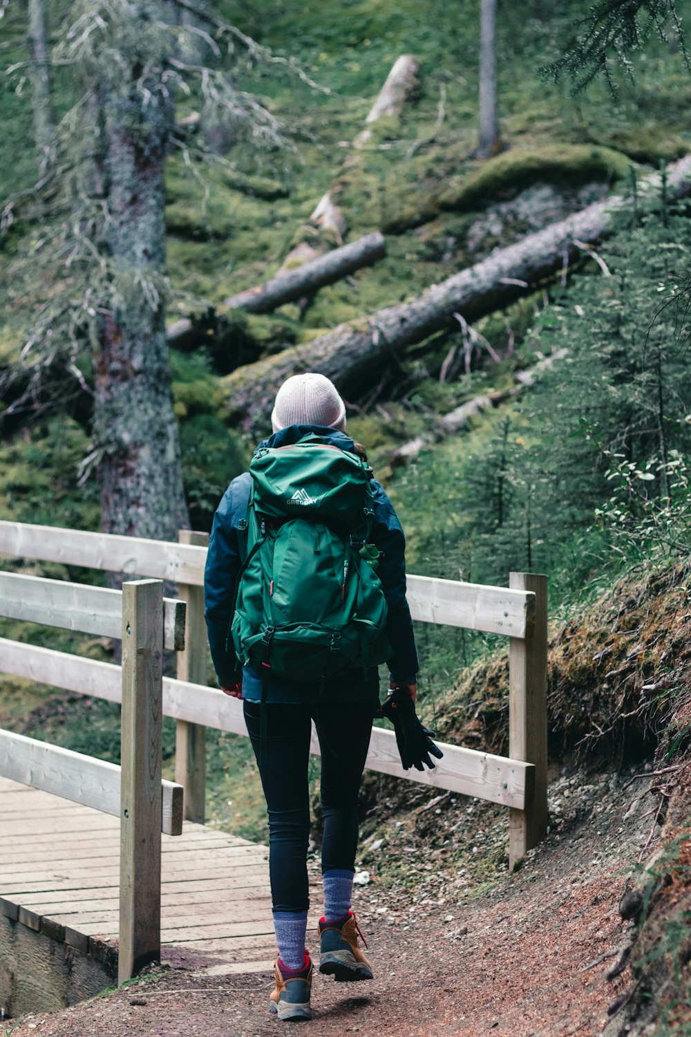 person in green and black jacket and black pants standing on brown wooden bridge during daytime