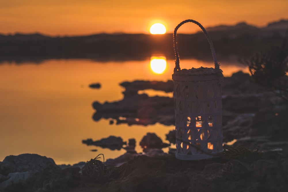 white and black basket on rock near body of water during sunset