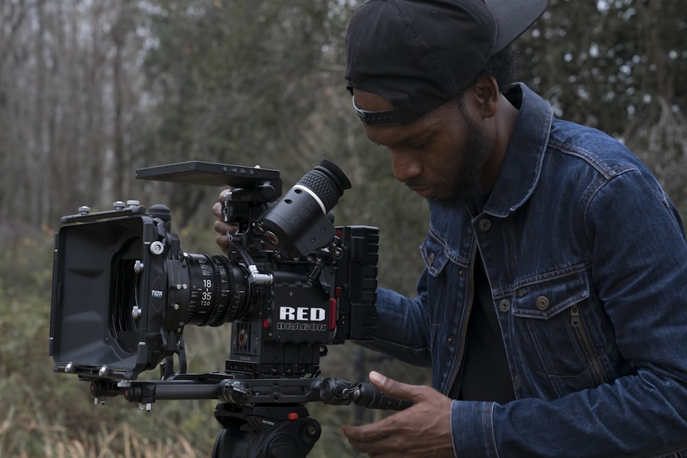 man in blue denim jacket holding black dslr camera