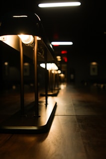 A row of elegant lamps is illuminated against a dark background, casting a warm glow on a wooden surface. The perspective of the shot gives depth, highlighting the sleek design and symmetry of the lamp fixtures.
