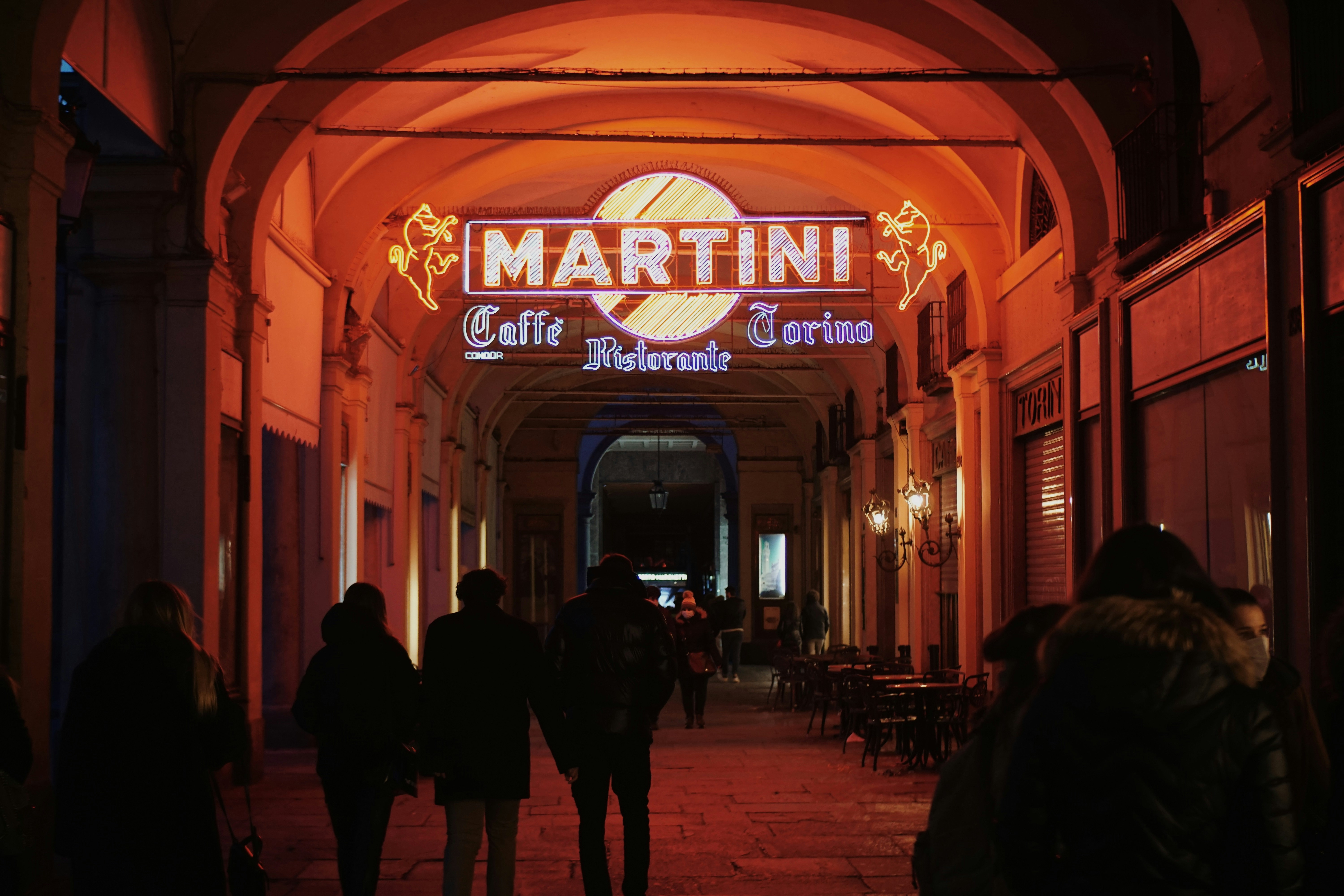 people walking on street during nighttime, Martini neon sign in Italian city 