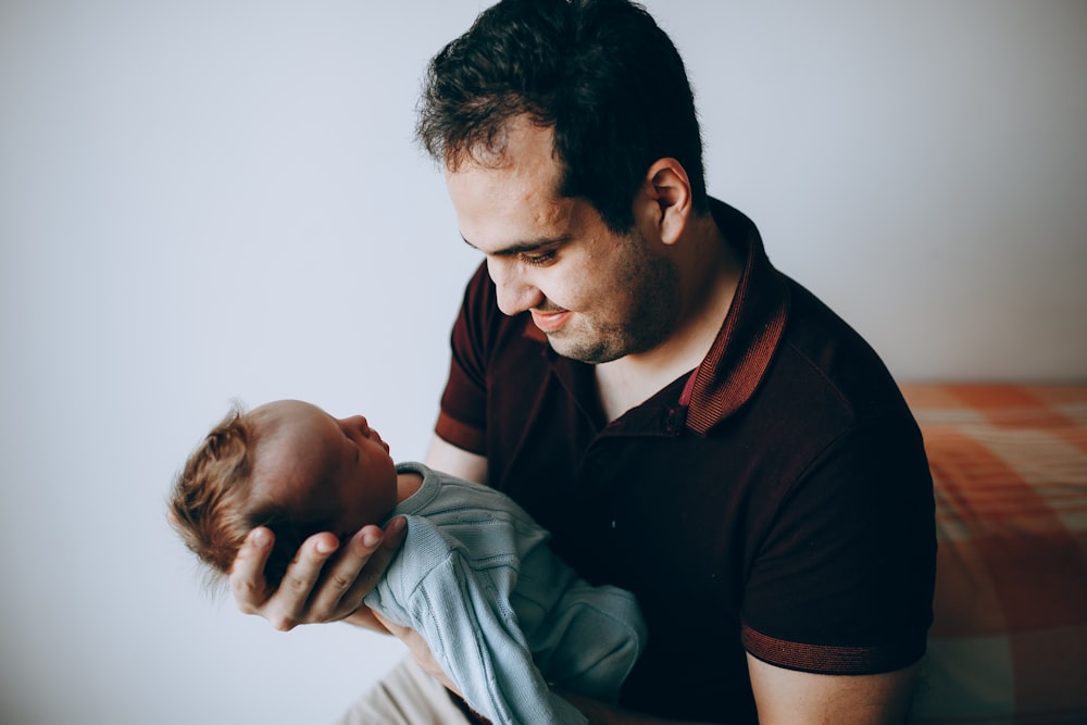 man in black polo shirt carrying baby