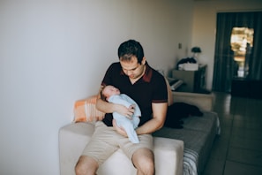 A happy new father reading the ebook on a cozy couch with baby toys around