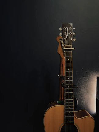 Softly lit studio corner with George tuning his acoustic guitar against a creamy off-white wall.