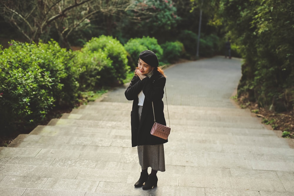 woman in black coat standing on sidewalk during daytime