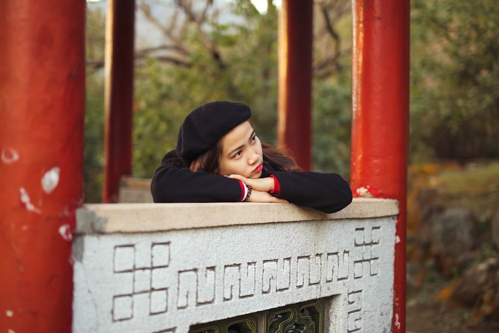 woman in black hoodie leaning on gray concrete wall during daytime