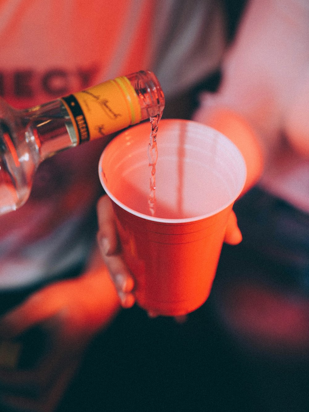 person pouring brown liquid on red plastic cup