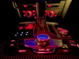 A car's central console with a gear shift lever and various buttons and knobs, all illuminated with red and blue backlighting. The buttons include options for navigation, media, telephone, menu, car, and more.